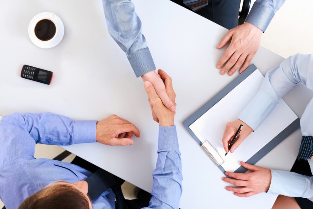 Un gruppo di uomini d'affari dalla mentalità aperta si stringono la mano attorno a un tavolo, suggellando l'accordo con ottimi prezzi.