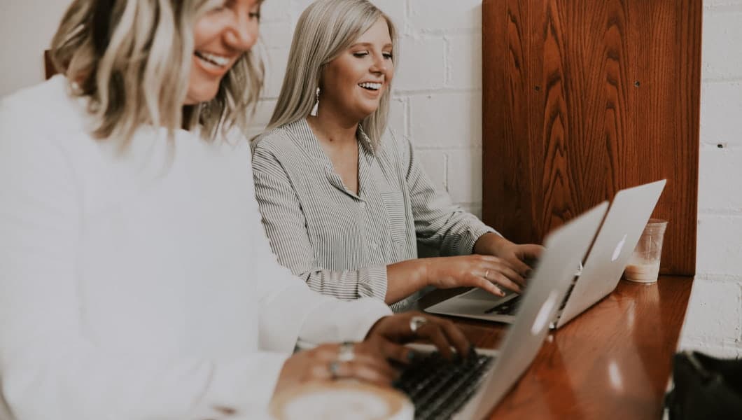 Due donne innovazione e impresa ridono e collaborano su un laptop in un ambiente di impresa informale.